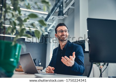 Bearded male business expert in glasses working with laptop in office while looking away