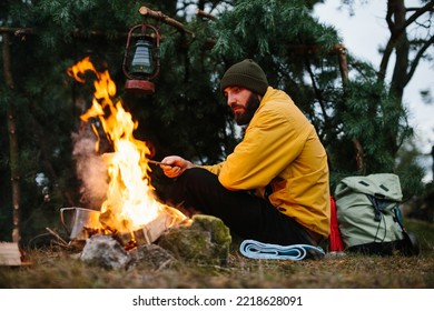 Bearded male hiker roasts sausages on a bonfire. Dinner in the wild, travel and survival concept. - Powered by Shutterstock