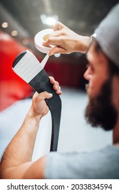 Bearded male ice hockey player wraps tape around hook hockey sticks to protect against impact and damage - preparing for a hockey game - Shutterstock ID 2033834594