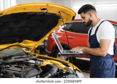 Bearded Male Mechanic Using Laptop, Recording Automobile Engine Checks Collect Detailed Information During His Work On Car Workshop. Service Maintenance During Engine Repair.