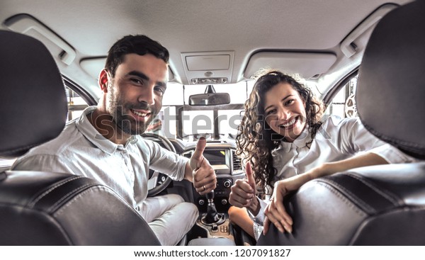 Bearded man and attractive brunette\
showing thumb up inside the new car at the\
dealership.