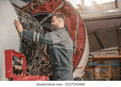 Bearded man aviation maintenance technician holding screwdriver and smiling while repairing aircraft