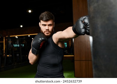 A bearded man in a black shirt trains in a gym, throwing punches at a heavy bag with black boxing gloves. - Powered by Shutterstock