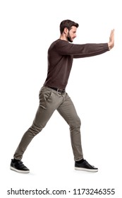 A bearded man in casual clothes tries to push a heavy object with both arms with one leg put in front for balance. Physical force. Test of strength. Man at work. - Shutterstock ID 1173246355