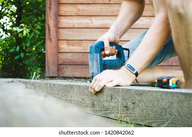 Bearded Man Is Choosing Electro Tool In A Hardware Store. He Is Taking Small Jig Saw From Heap With Sale And Examining It