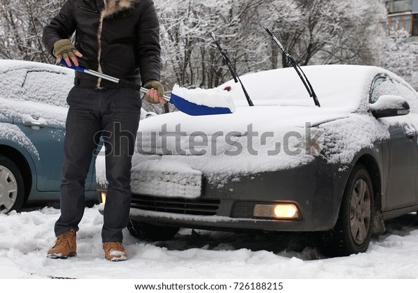 bearded\
man cleans snow from a car on a winter\
morning
