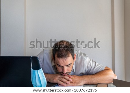 Bearded man dejected in front of the computer wearing a mask to protect himself from the coronavirus. Frustration concept