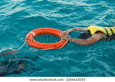 A bearded man diver in a life jacket holds on to a lifebuoy in transparent azure sea water.