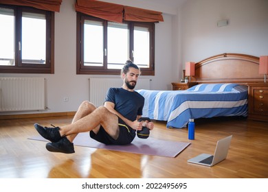 Bearded Man Doing Kettlebell Russian Twist To Work Out At Home While Watching An Online Class On The Laptop.