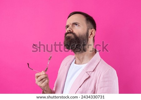Bearded man dressed in a pink jacket with glasses. Emotional studio portrait.
