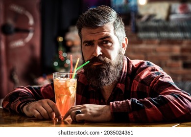 Bearded Man Drinks Cocktail At The Bar.Handsome Barber Resting At Night Club. Bearded Brutal Hipster Thinking Aout Life.Non Alcoholic Fresh Tropical Cocktail. Alone Bearded Man Sitting At Bar Counte