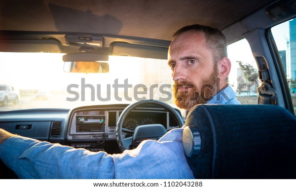 A bearded man driving an old car in the rays of\
the setting sun. Portrait.