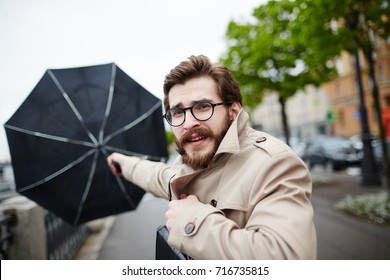 Bearded man in eyeglasses and trench-coat holding his umbrella in stormy weather - Powered by Shutterstock