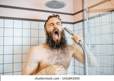 Bearded man feeling shocked while taking a shower with cold water in the bathroom at home