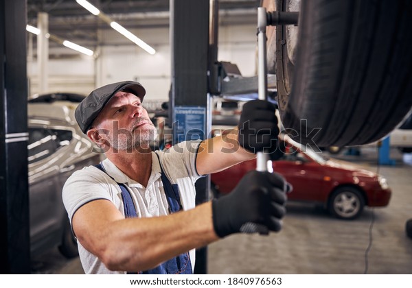Bearded man in gloves\
tightening bolts on wheel with torque wrench while working in\
automobile repair\
garage