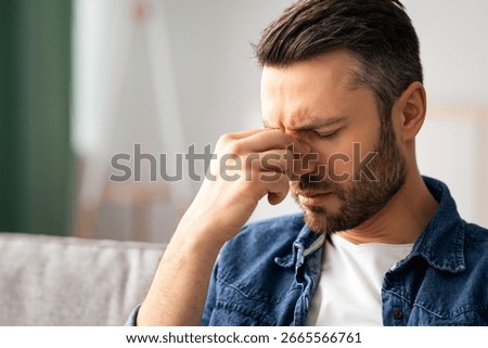 Bearded man having headache, touching his nose bridge