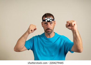 A Bearded Man With A Headlamp In A Hat Raising His Fists In Ostility, Isolated On Beige Background