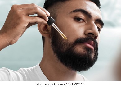 Bearded man holding pippete with beard oil