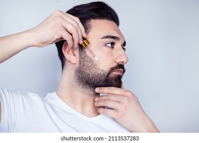 Bearded man holding pippete with beard oil	