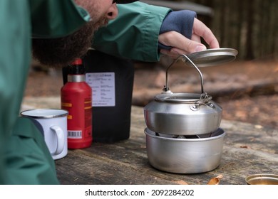 Bearded Man Impatiently Waiting For His Coffee To Boil In A Camping Kettle Outside In The Forest With His Mug Ready To Be Filled