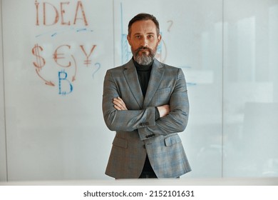 Bearded man in a jacket standing in front of wall with whiteboard