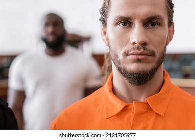 Bearded Man In Jail Uniform Looking At Camera Near Blurred African American Juryman