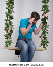 Bearded Man In Jeans, Swinging On Swings And Hamming To The Camera. Wooden Swing Suspended From A Rope Hemp, Rope Wrapped Vine And Ivy. Different Emotions