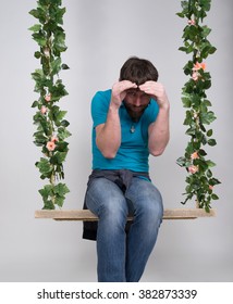 Bearded Man In Jeans, Swinging On Swings And Hamming To The Camera. Wooden Swing Suspended From A Rope Hemp, Rope Wrapped Vine And Ivy. Different Emotions