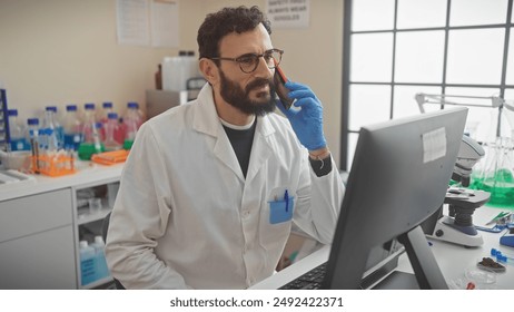 A bearded man in a lab coat talks on a phone in a laboratory with scientific equipment. - Powered by Shutterstock