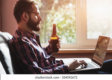 bearded man with laptop drinking bottle of beer - Powered by Shutterstock