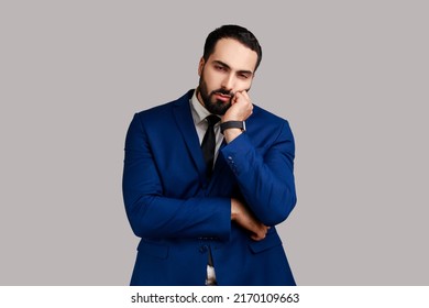 Bearded Man Leaning On Hand And Looking At Camera With Disinterest, Listening To Boring Story, Disappointed With Result, Wearing Official Style Suit. Indoor Studio Shot Isolated On Gray Background.