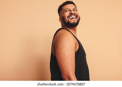 Bearded man looking away with a smile on his face in a studio. Happy young man standing alone against a studio background. Body positive man feeling comfortable in his natural body.