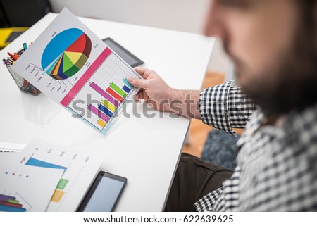 Bearded man looking at graph document in office, part of