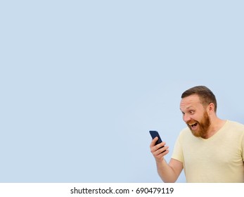 Bearded Man looking into the phone rejoices photo to advertise a lot of space under the text. Dressed in a yellow T-shirt on a blue background
