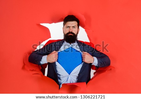 Bearded man looking through paper. Through paper. Super businessmen in red cape showing blue shirt. Save the world. Superhero. Red Superman Cape. Safety hero. Symbol S. Business growth. Super power.