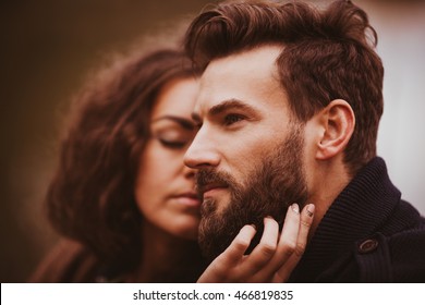 Bearded man looks far away while lovely brunette strokes his face