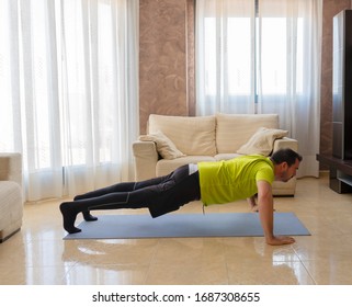 Bearded man in low shape exercising with black and green sportswear in his living room in front of the sofas on a mat - Shutterstock ID 1687308655