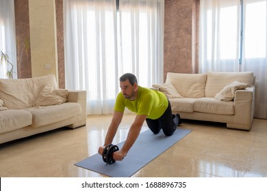 Bearded man in low shape exercising with black and green sportswear in his living room in front of the sofas on a mat - Shutterstock ID 1688896735