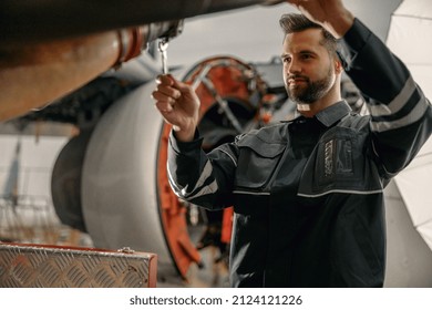 Bearded man maintenance technician using wrench tool while repairing aircraft at repair station