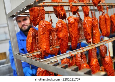 A Bearded Man A Meat-packing Plant Worker Carries A Rack With Hanging Meat Delicacies From Pork In A Tomato Marinade With Sesame Seeds