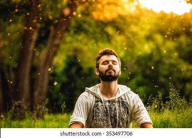 A bearded man is meditating on green grass in the park with face raised up to sky and eyes closed on sunny summer day. Concept of meditation, dreaming, wellbeing and healthy lifestyle