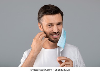 Bearded Man Moved Protective Medical Mask From Face To Scratch Beard, Grey Studio Background, Free Space. Do Not Touch Your Face, Avoid Touching Your Face During Pandemic, Stay Safe During Lockdown