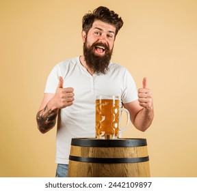 Bearded man with mug of beer on wooden barrel showing thumbs up. Happy brewer with glass of lager beer. Equipment for preparation of beer. Beer pub and bar. Handsome bearded man drinking fresh ale. - Powered by Shutterstock