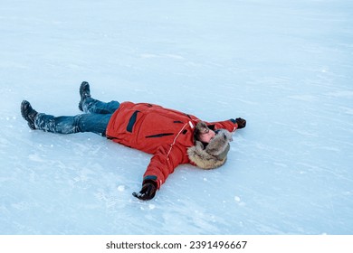a bearded man in an orange jacket lying on the ice. a man on an ice rink
