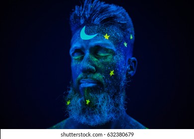 Bearded man painted neon paint under UV light. Beauty image human space, neon sleep man in stars on black background, blue on black.
