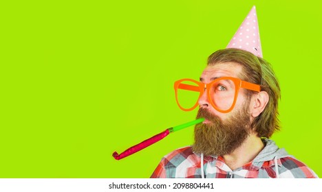 Bearded Man In Party Hat Blow Noisemaker. Happy Guy In Big Glasses In Birthday Cone Cap. Copy Space.