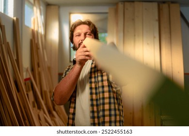 Bearded man in a plaid shirt inspecting a wooden board in a workshop for his new piece of furniture. - Powered by Shutterstock