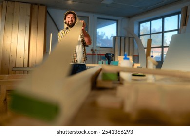 Bearded man in a plaid shirt inspecting a wooden board in a workshop for his new piece of furniture. - Powered by Shutterstock