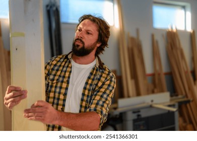 Bearded man in a plaid shirt inspecting a wooden plank in a workshop for his new piece of furniture. - Powered by Shutterstock