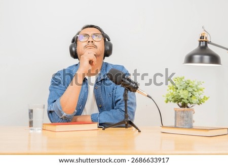 Bearded man podcaster looking up while thinking with headphones at home podcast studio.